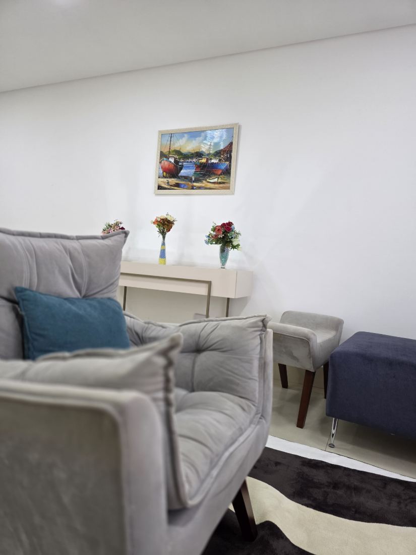 Sala de atendimento com poltronas cinza, almofada azul e quadro na parede